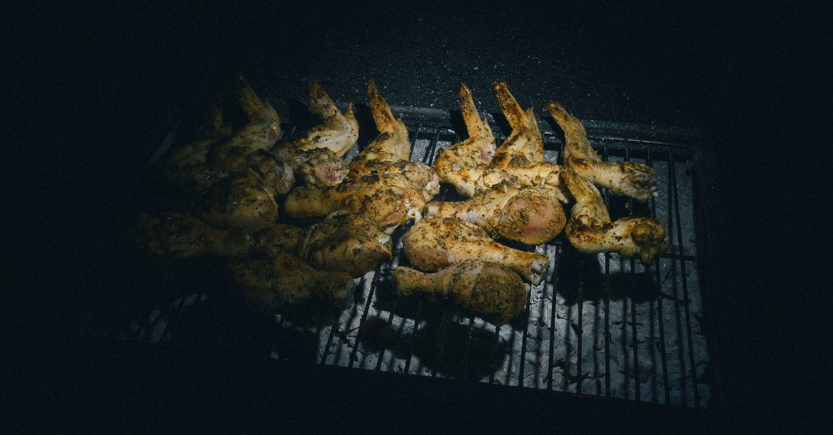 Tasty chicken wings being grilled under low light on a barbecue at night.